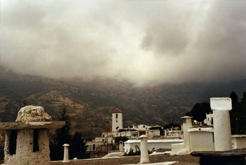 Foto zeigt ein Dorf und Hügel von Wolken umgeben.